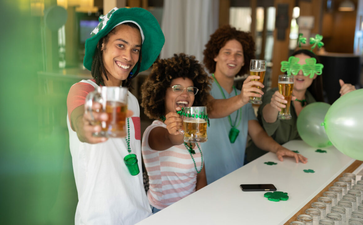 Diverse Group Of Happy Friends Celebrating St Patrick’s Day Raising Glasses Of Beer At A Bar. Fun During Celebration Of The Irish Patron Saint’s Day.